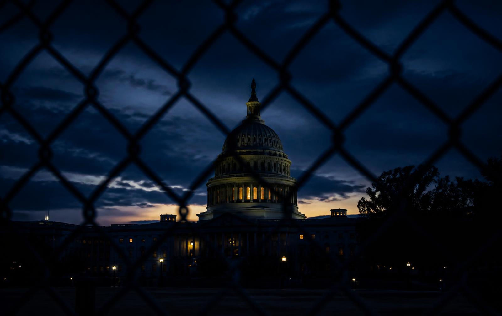 The United States Capitol at dusk seen through a chain-link fence